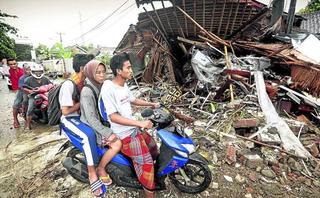 Imagen principal - Vecinos de Pandeglang abandonan en motocicletas sus viviendas arrasadas por el agua. Abajo, los equipos de rescate recuperan los cuerpos de las víctimas.