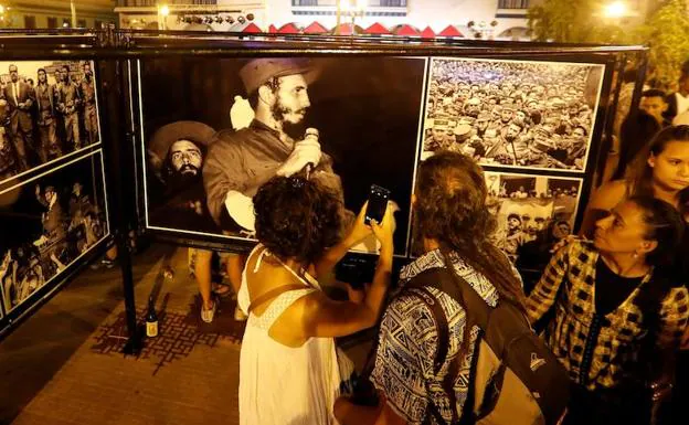 Turistas y residentes en Santiago de Cuba conversan frente a una exposición de fotografías referentes a momentos de la Revolución cubana. 