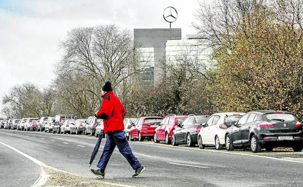 Un hombre camina por las inmediaciones de la fábrica, con numerosos vehículos estacionados en el arcén.