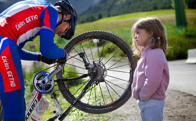Un ciclista arregla la cadena de su bici bajo la atenta mirada de una niña.