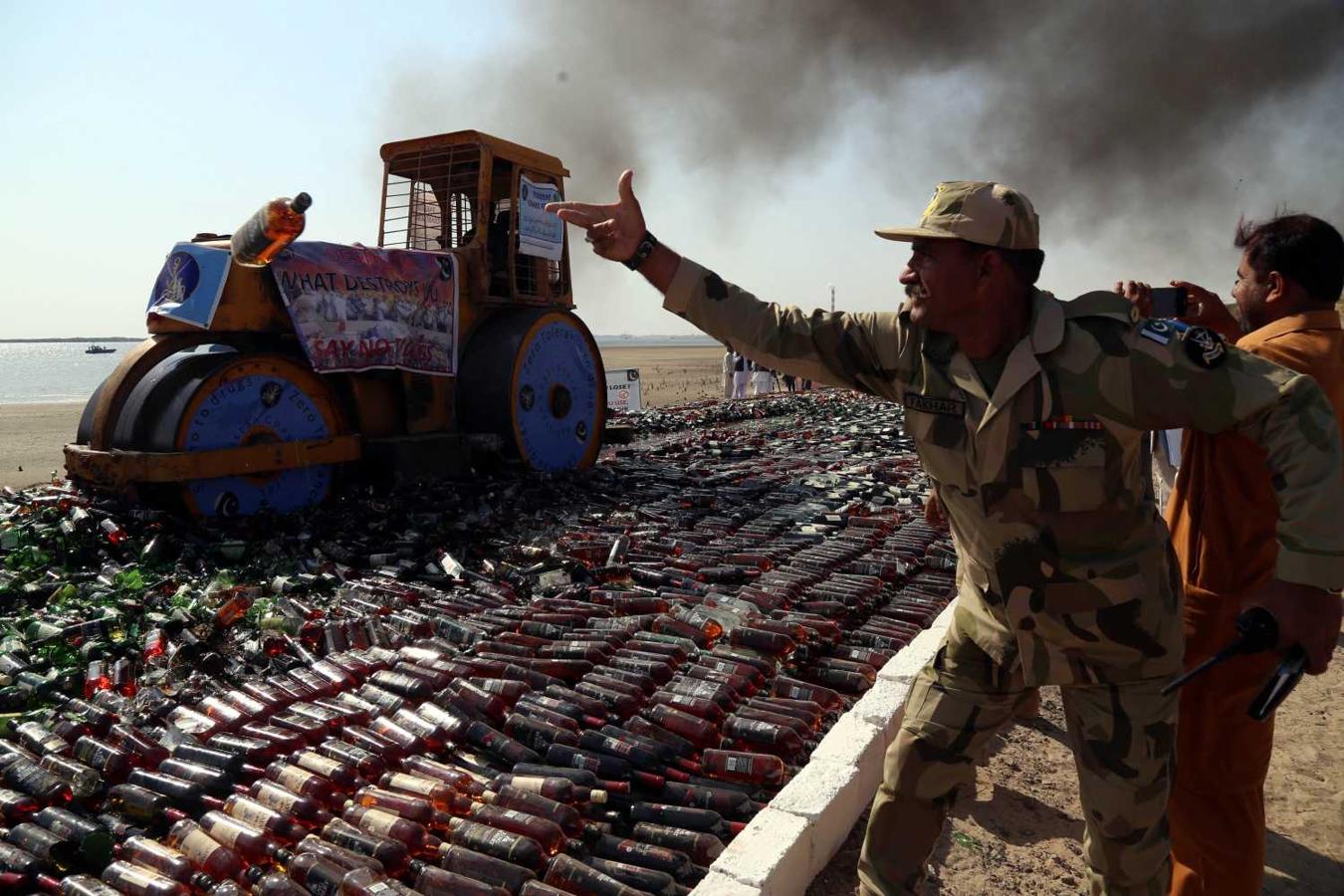 Miembros de las autoridades paquistaníes destruyen botellas de licor incautadas, en Karachi, Pakistán