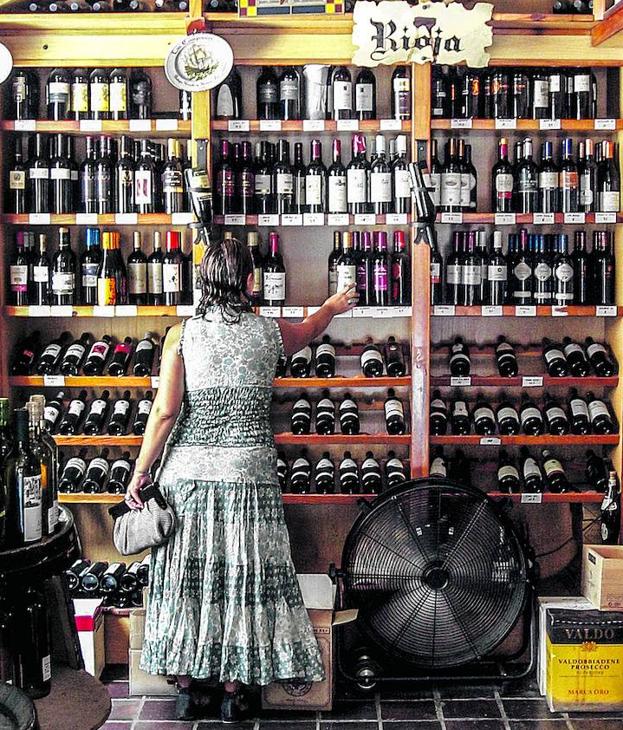 Una mujer elige un vino en una estantería llena de botellas.