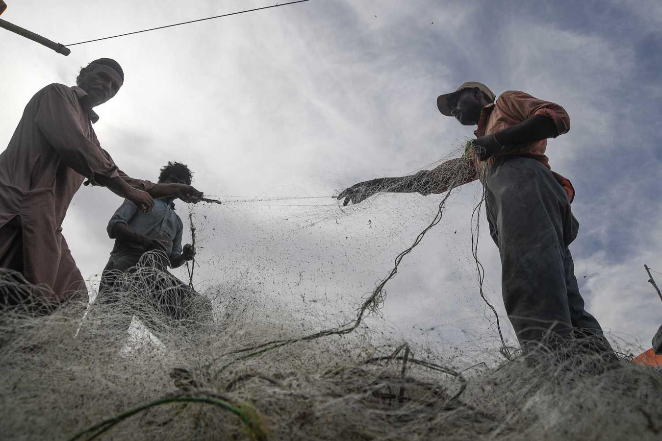 Pescadores pakistaníes preparan su red de pesca en un barco, en un puerto en Karachi