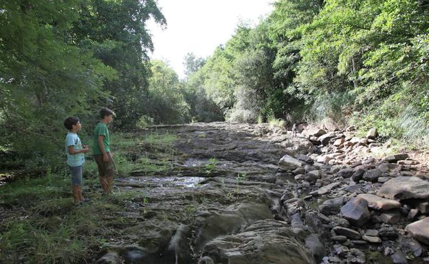 Unos niños contemplan el cauce prácticamente seco del arroyo Mape en Busturia en verano.