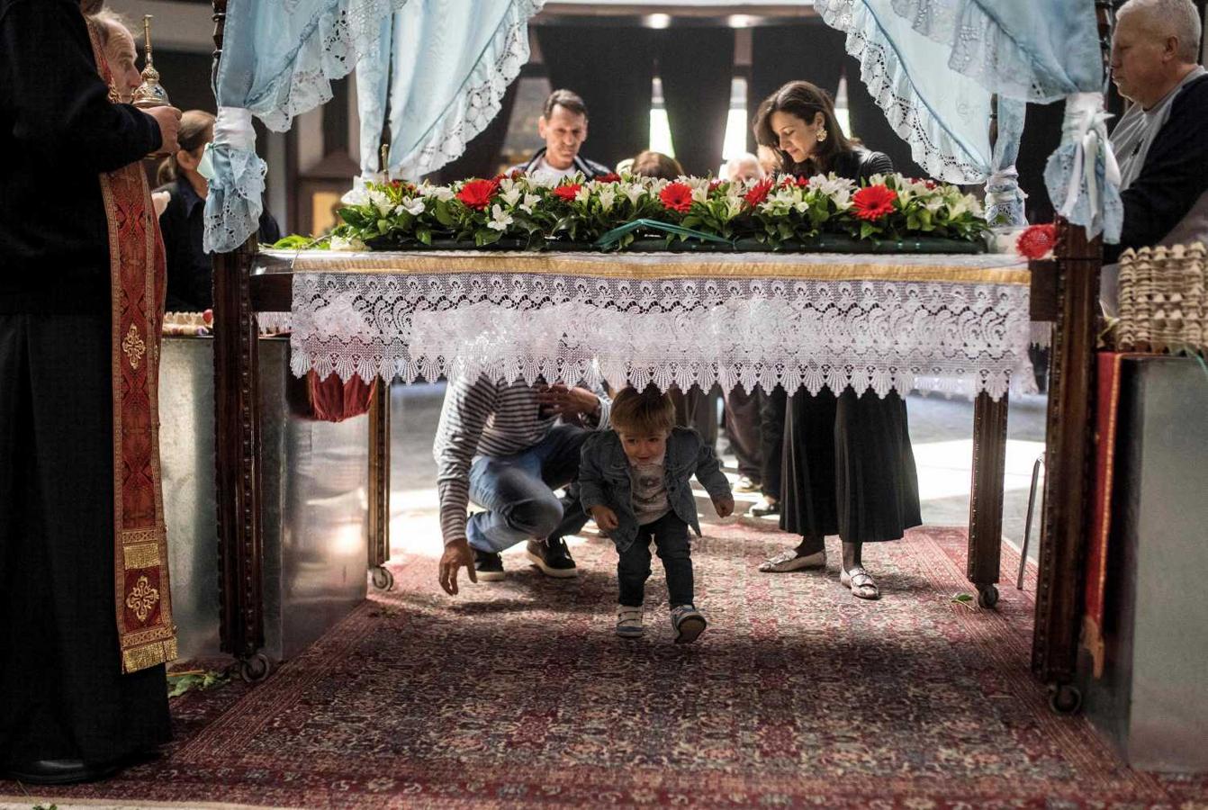 Cura ortodoxo bendiciendo a un niño mientras pasa por debajo de la mesa que simboliza la tumba de cristo, durante la celebración de la procesión de Viernes Santo, en Skopje, Macedonia 