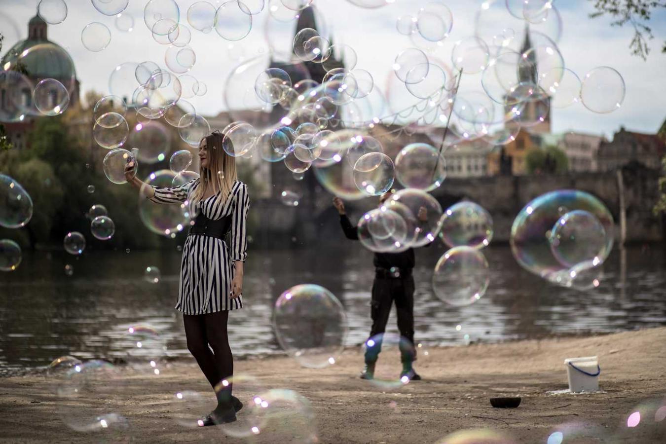 Una chica se hace un selfi rodeada de las burbujas que hace flotar en el aire un artista callejero a orillas del río Moldava, en Praga, República Checa. 