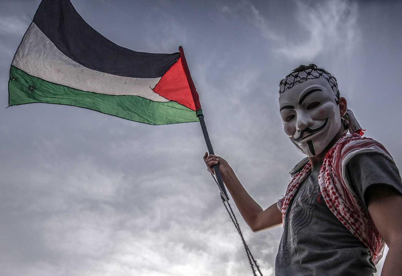 Un protestante con la máscara de Guy Fawkes porta una bandera palestina durante la jornada de protestas contra Israel, hoy en la ciudad cisjordana de Gaza. 