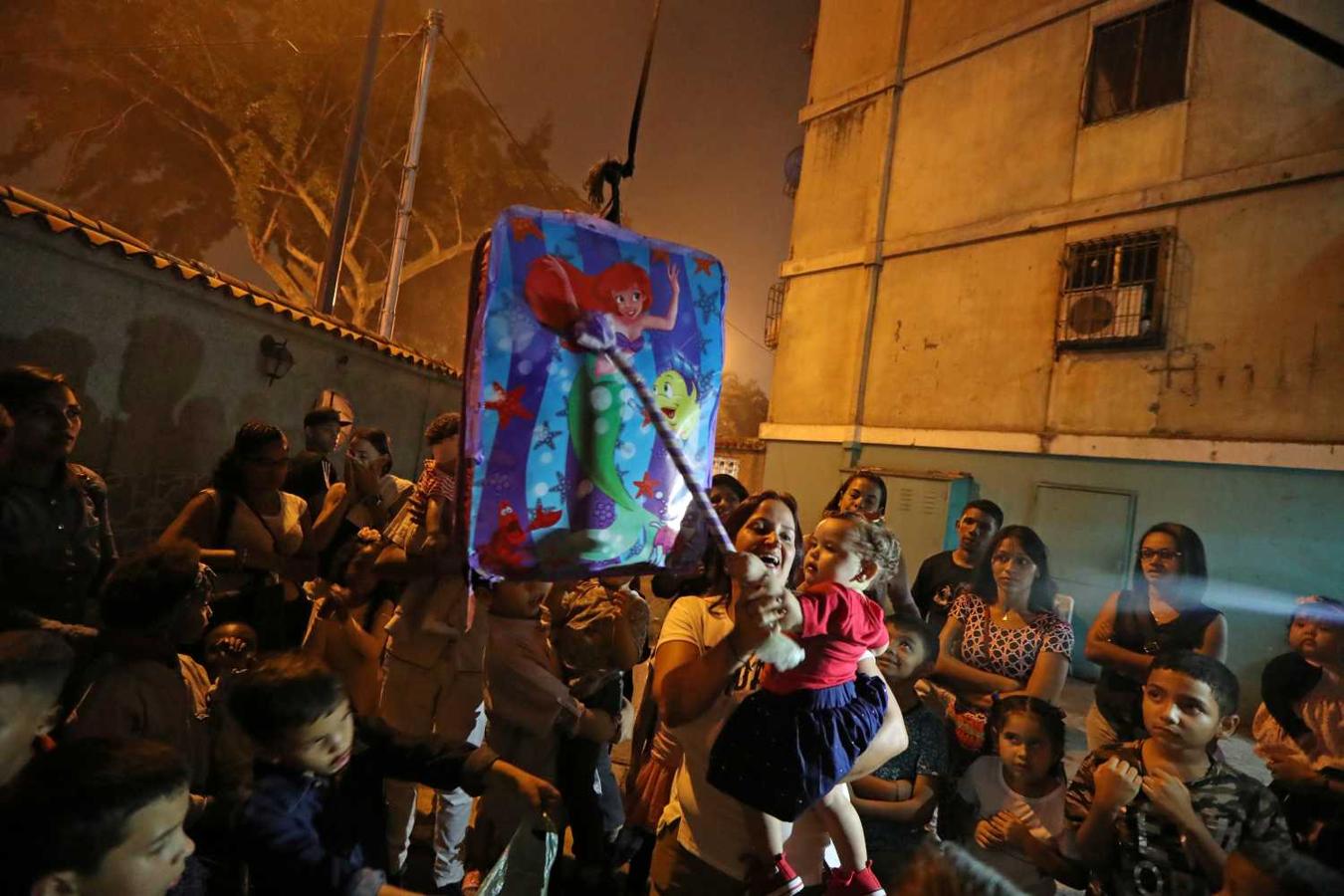 Una mujer sostiene a un niño mientras se preparan para golpear una piñata en una fiesta de cumpleaños en Caracas, Venezuela.