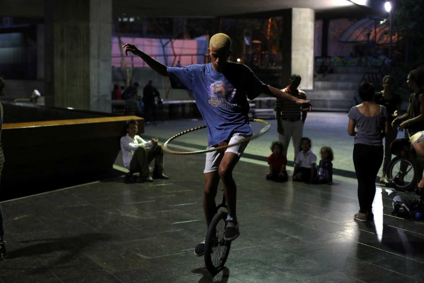 Un joven practica en un monociclo mientras gira un hula hoop en el área del teatro Teresa Carreno donde los amigos se reúnen para practicar en Caracas, Venezuela