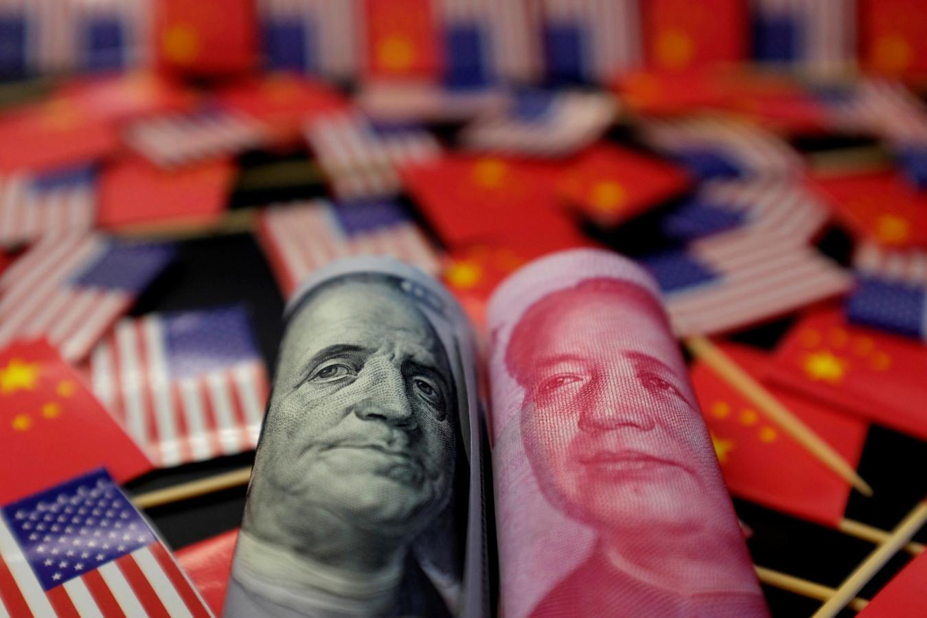 Un billete de dólar estadounidense con el padre fundador estadounidense Benjamin Franklin y un billete de yuan chino con el fallecido presidente chino Mao Zedong aparecen entre las banderas de Estados Unidos y China