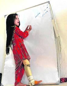 Imagen secundaria 2 - Arriba, algunos de los niños caminando delante de Hamisha Gul, el patriarca. A la izquierda, junto a la abuela Niaz Bibi, armada con un fusil. Y a la derecha, la pequeña Marwa, de seis años, que perdió a su madre, su hermana gemela y a dos de sus primos, escribiendo en la rudimentaria pizarra que tienen en casa.