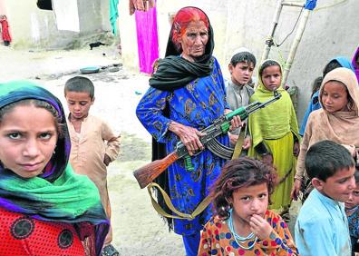 Imagen secundaria 1 - Arriba, algunos de los niños caminando delante de Hamisha Gul, el patriarca. A la izquierda, junto a la abuela Niaz Bibi, armada con un fusil. Y a la derecha, la pequeña Marwa, de seis años, que perdió a su madre, su hermana gemela y a dos de sus primos, escribiendo en la rudimentaria pizarra que tienen en casa.