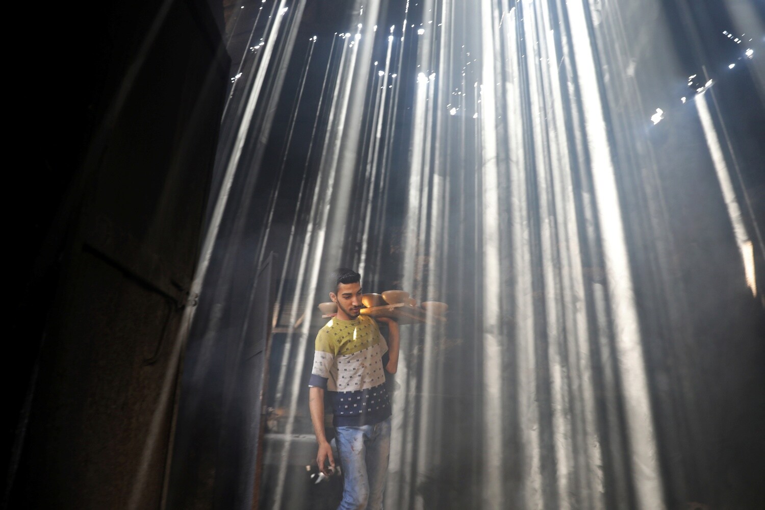 Un trabajador palestino lleva ollas de barro mientras los rayos del sol penetran en el techo de un taller de cerámica en la ciudad de Gaza