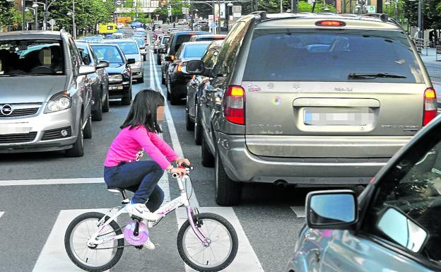 Una niña cruza en bicicleta por el paso de cebra de una calle de Bilbao repleta de vehículos en caravana.