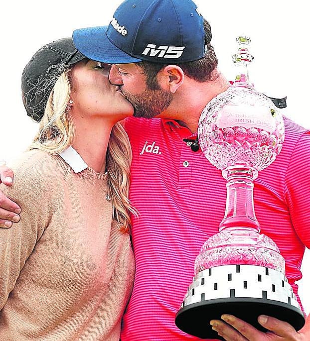 Rahm sujeta el trofeo y besa a su prometida, Kelley Cahill.