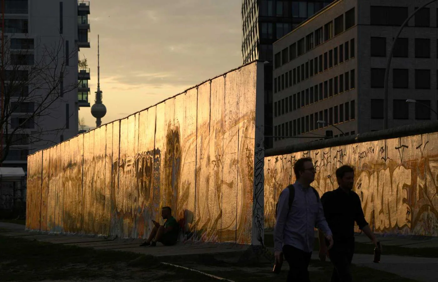 La gente pasea por la East Side Gallery cerca del río Spree durante el atardecer en Berlín