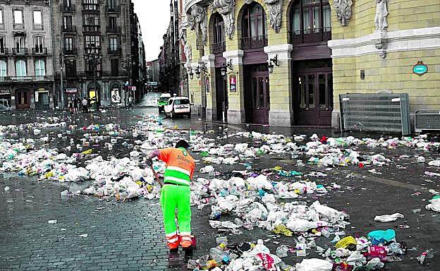 Un operario del servicio municipal de limpieza barre cientos de botellas y bolsas de plástico a primera hora de la mañana en la plaza del Arriaga.