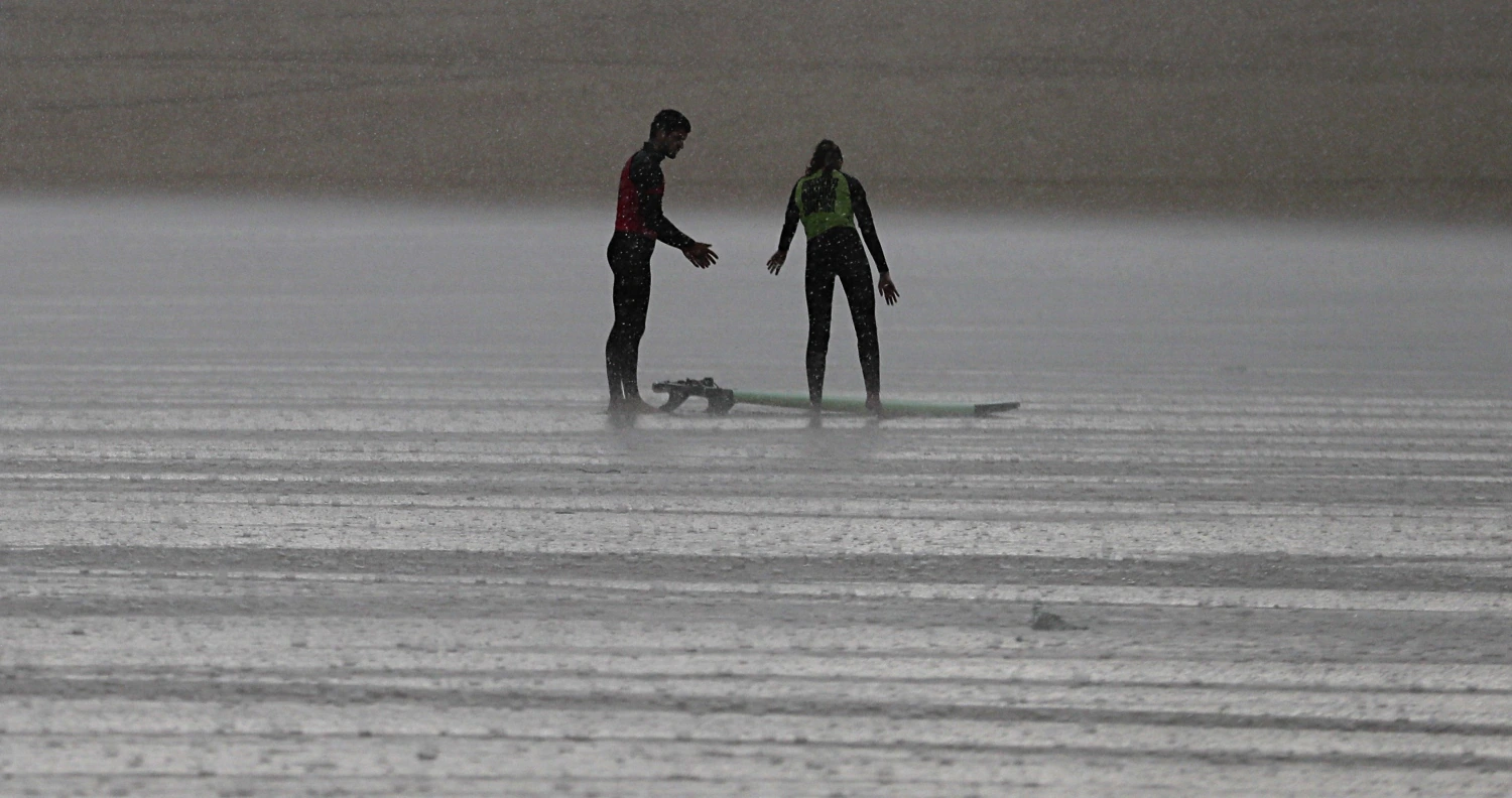 Unos jóvenes se preparan para hacer surf en la playa de la Zurriola de San Sebastián bajo un fuerte aguacero. 