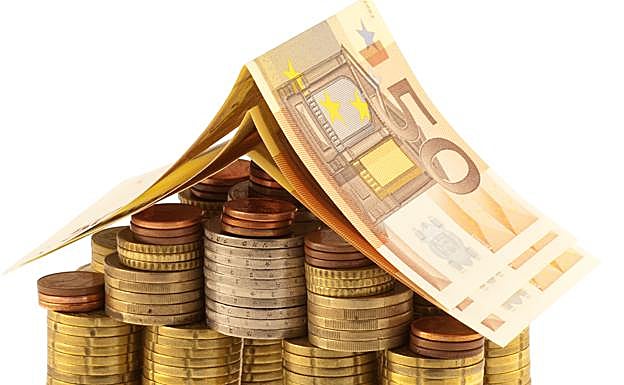 Montones de monedas y billetes de euro colocados de forma que representan una casa