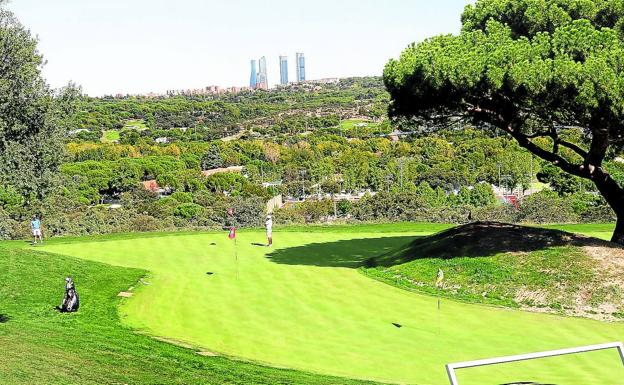 Imagen de uno de los putting green junto al hoyo 1 del Club de Campo, con la silueta de 'Las Cuatro Torres' perfilando el skyline del nuevo Madrid.