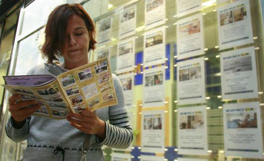 Una mujer consulta un folleto junto a una inmobiliaria. 