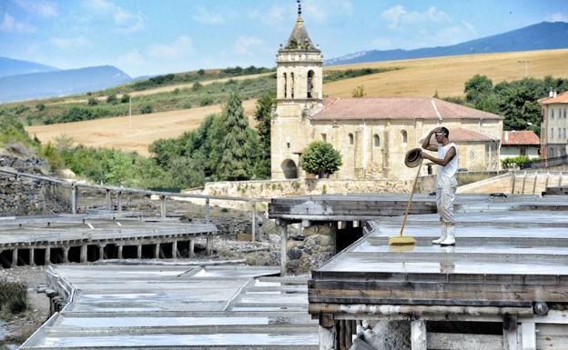 Un salinero trabaja en las eras, con la iglesia de Salinas de Añana al fondo. 