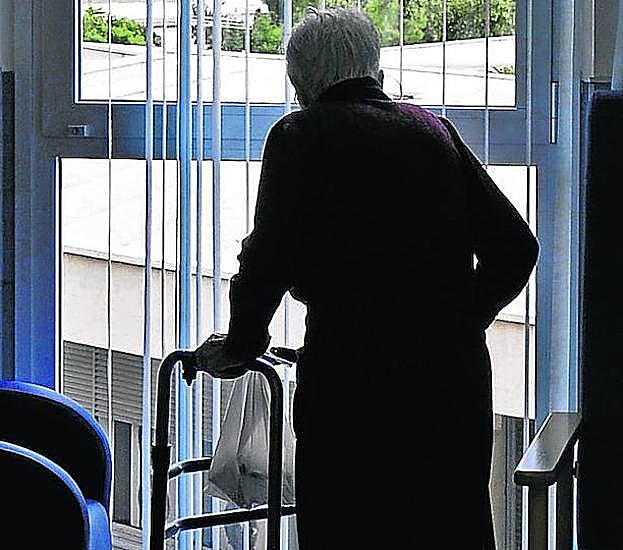 Una persona mayor mira por la ventana en un centro residencial. 