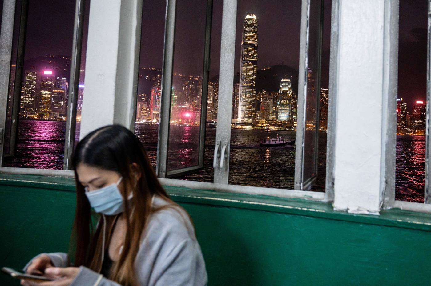 Una mujer con una máscara facial mira su teléfono móvil mientras espera un ferry en el lado de Kowloon de Hong Kong. 