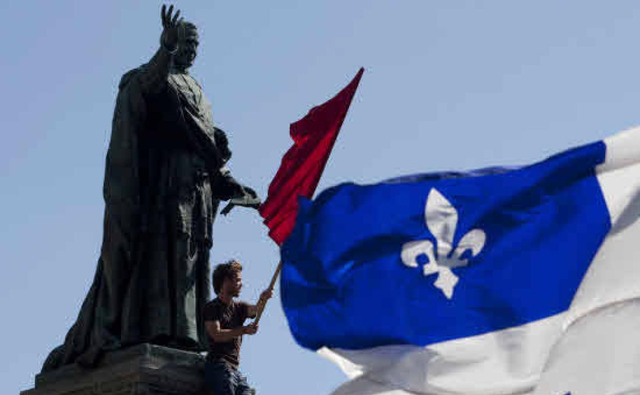 Gazte batek Quebeceko banderaren ondoan dagoen Montrealgo estatua batera igonda. 