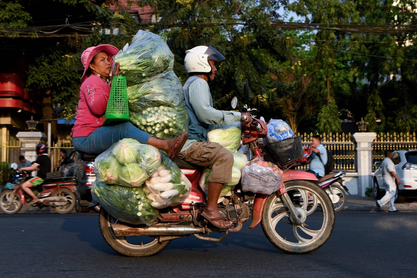 Una mujer sostiene montones de vegetales transportados en motocicleta por una calle en Phnom Penh, Camboya 