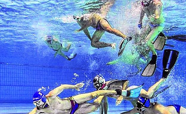 Varios jugadores persiguen a un delantero que empuja con un 'stick' la pastilla por el suelode la piscina en direccióna la portería del equipoadversario.