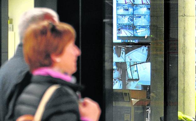 Una pareja pasa frente a la sala acristalada de visionado, donde un guardia de seguridad observa las imágnees de los monitores.