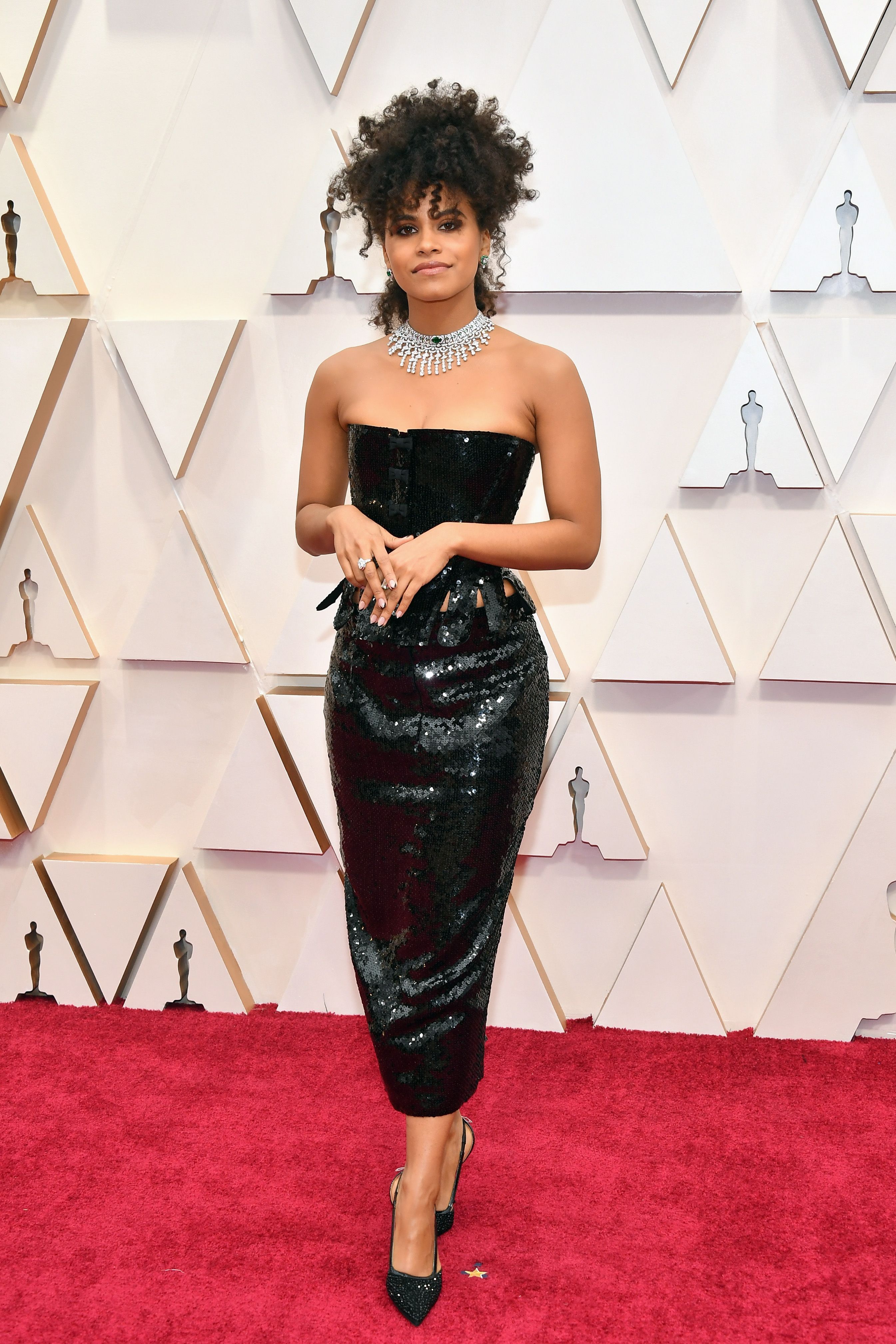 Zazie Beetz, la actriz de Joker, ha prescindido de traje largo de gala y ha apostado por un dos piezas de 'paillettes', compuesto por una falda de corte ‘midi’ ‘ y un cuerpo con flecos y escote palabra de honor tipo corpiño que no acabamos de ver adecuado para una alfombra roja de estas características.