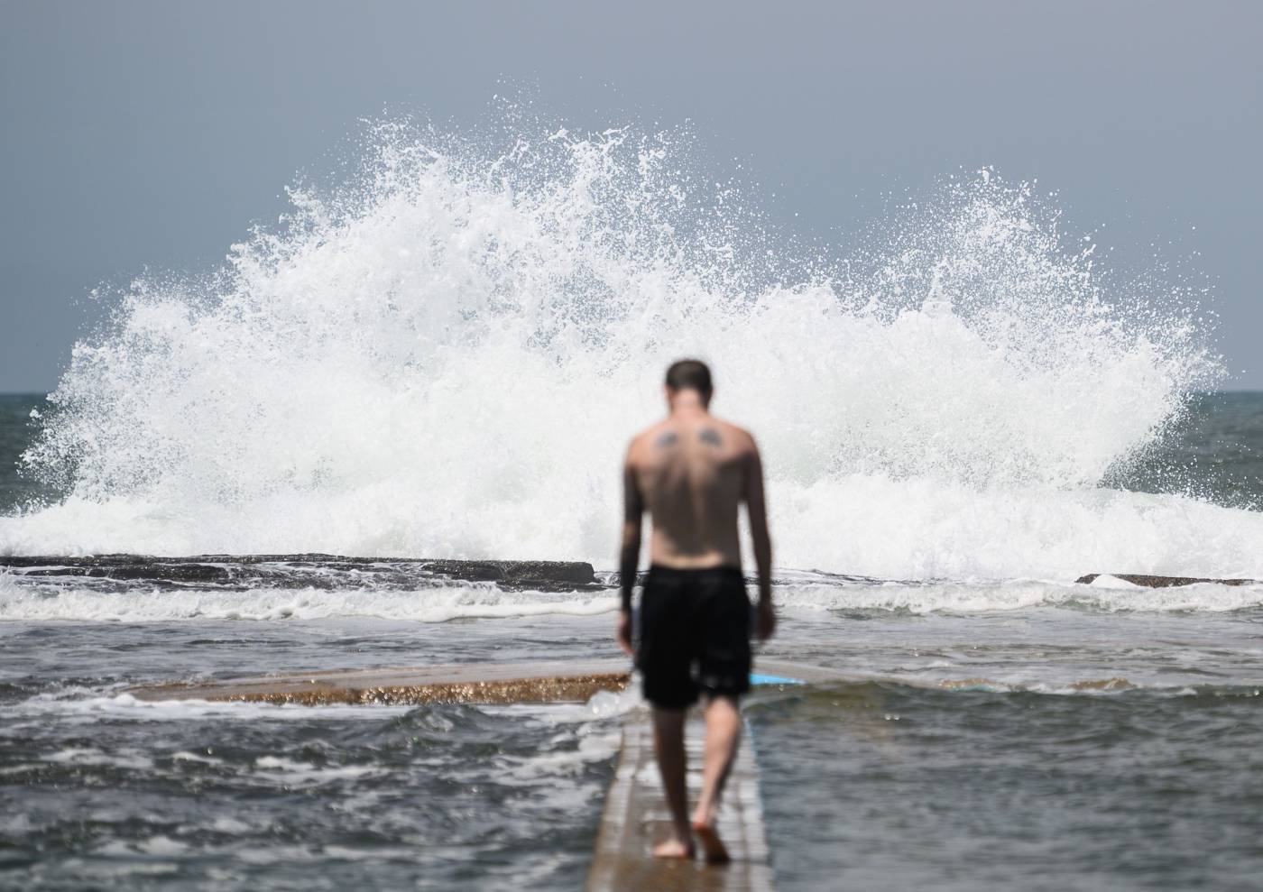 Un hombre camina en dirección a las olas sobre el dique que separa el mar de la piscina pública North Narabeen Rockpool, en una playa del norte de Sídney, en el estado de Nueva Gales del Sur (Australia). 