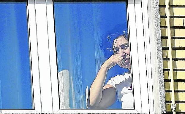 A la derecha, una vecina de la zona observa la calle con la ventana cerrada.