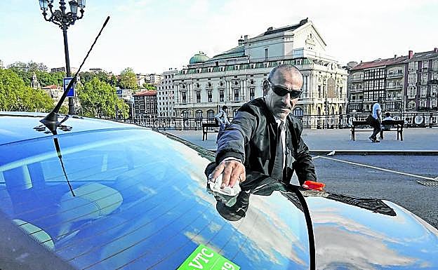 Un conductor de VTC limpia su vehículo estacionado cerca del Teatro Arriaga.
