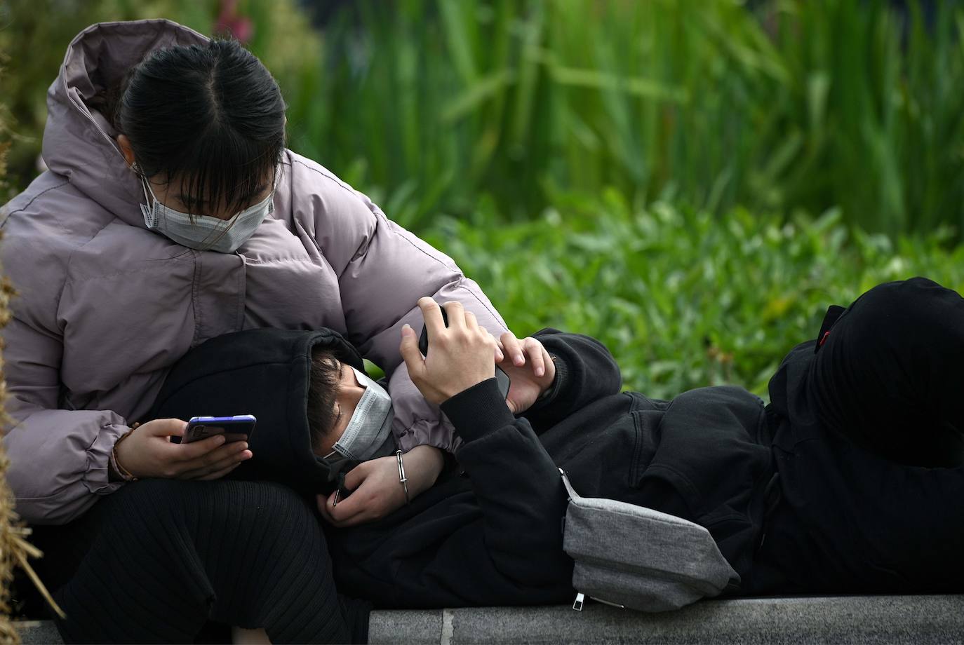 Una pareja protegida con mascarillas se sienta frente a la estación de ferrocarril en Hefei.