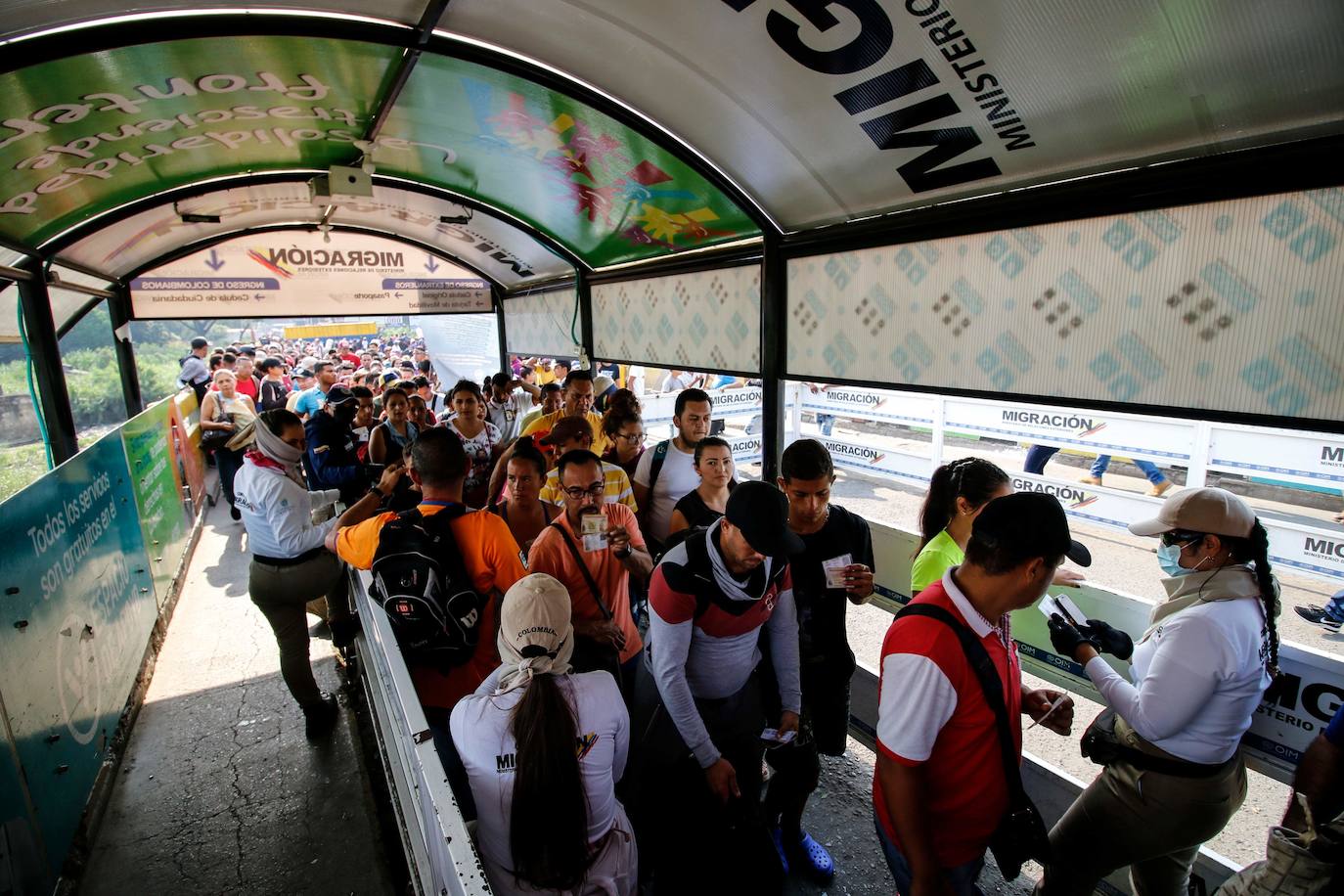 Funcionarios de migración usan mascarillas protectoras y cubren su boca y nariz con pañuelos para evitar contraer el nuevo coronavirus mientras revisan los documentos de las personas en el Puente Internacional Simón Bolívar, en Cúcuta.