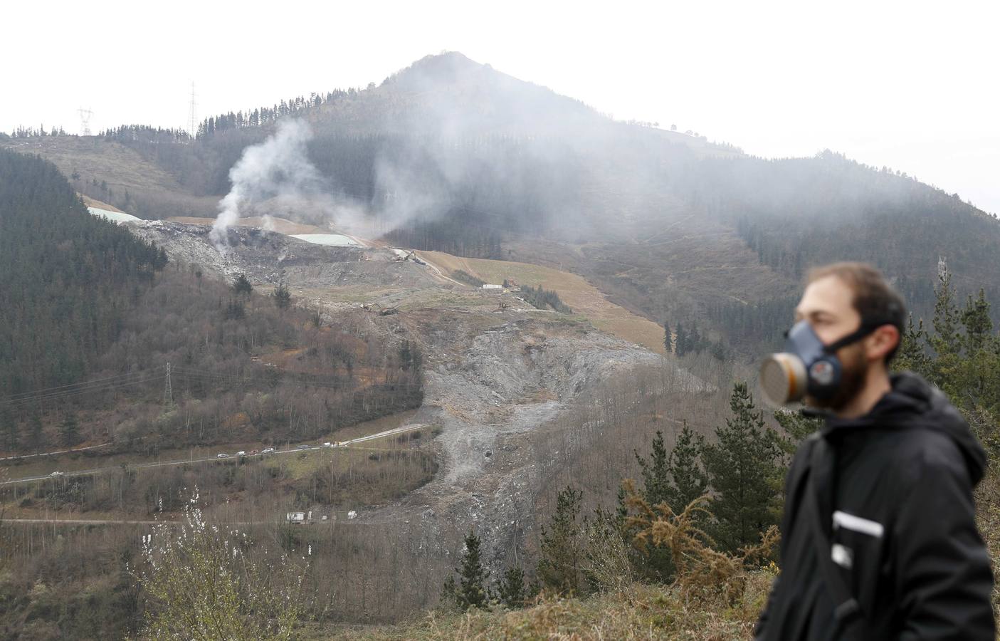 Un reportero de televisión protegido, en Ermua, con el fuego en el vertedero de fondo. El asunto llegó a los medios nacionales, sobre todo, cuando se hicieron públicos los primeros análisis sobre la pobre calidad del aire.. 