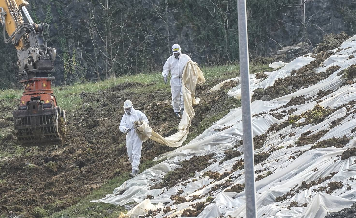 Operarios con las medidas de seguridad trabajan en la estabilización del terreno, donde se acumulan residuos con amianto.