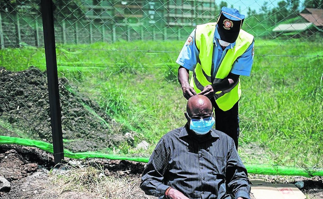 Un guarda se seguridad coloca una mascarilla a un anciano en el hospital de Nairobi.