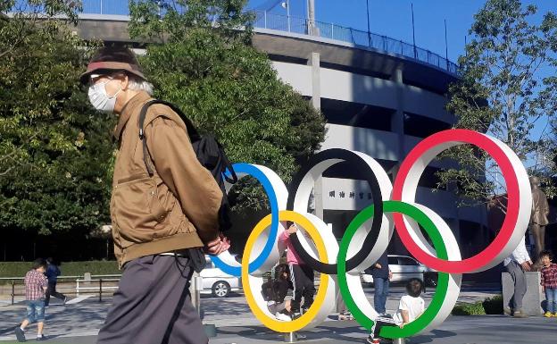 Una persona camina con una máscara delante de los anillos olímpicos en Tokio.