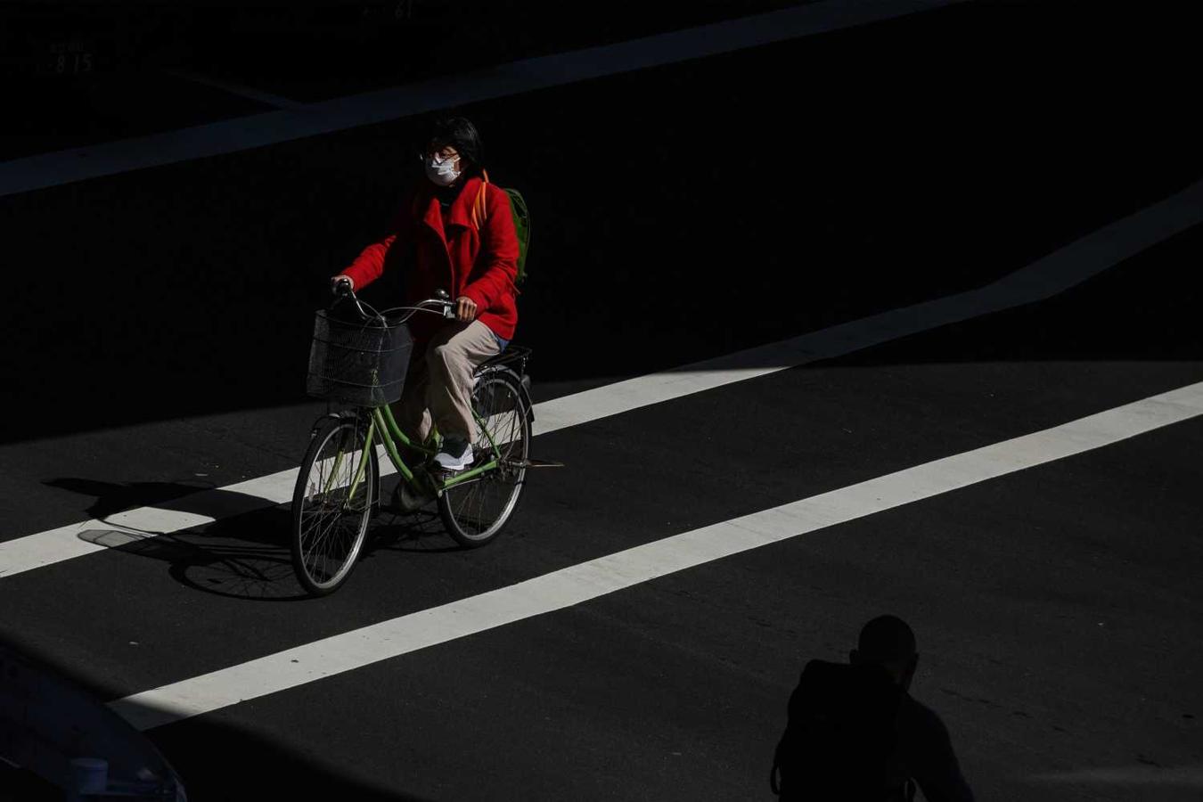 Una mujer con mascarilla y en bicicleta en una calle de Tokio