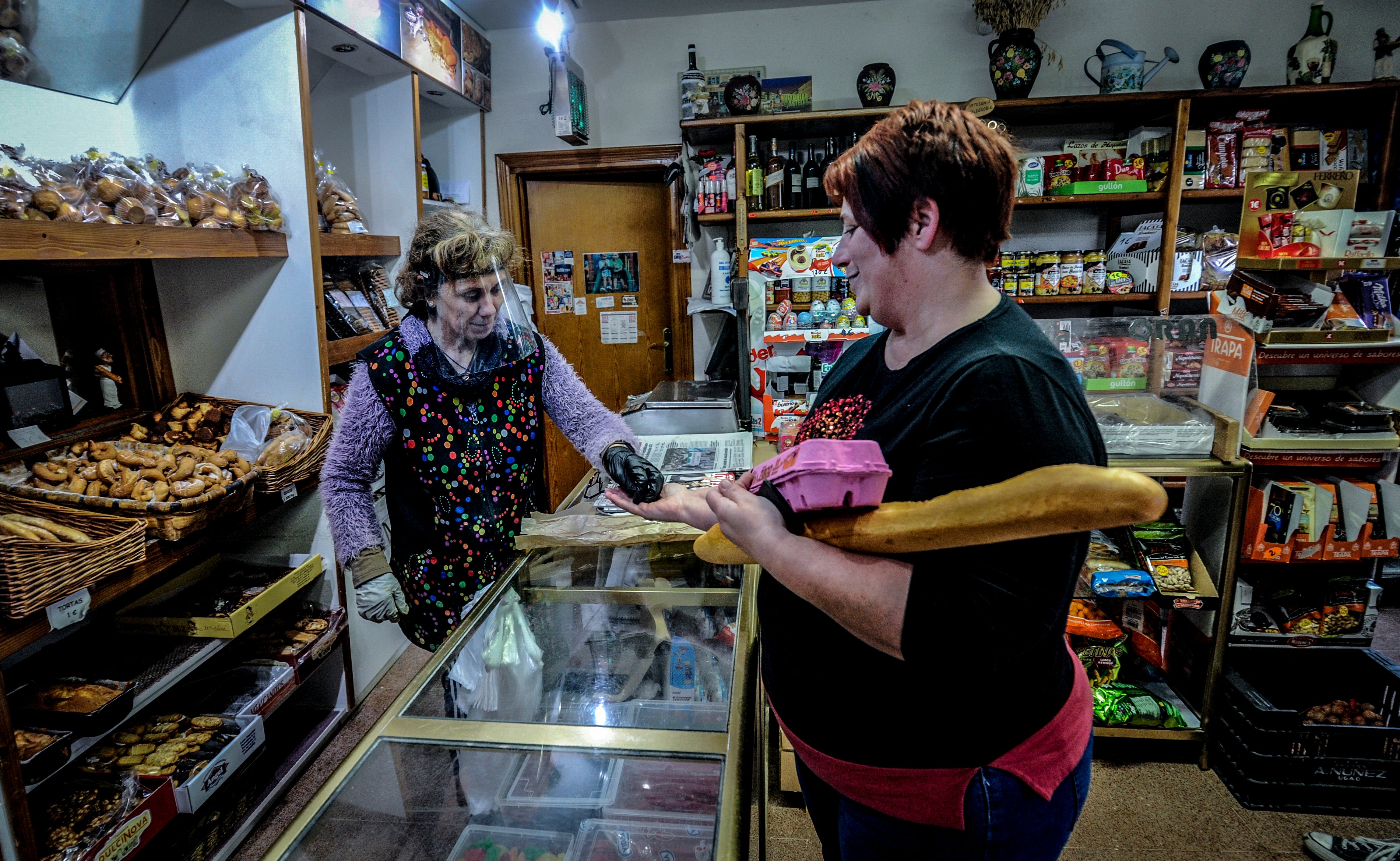 Maribel Bolinaga, a la izquierda, despacha pan y huevos a buen ritmo detrás de la pantalla protectora que ella misma ha fabricado y a la que denomina «el invento». Su panadería es una de las tiendas más ajetreadas de Espejo.