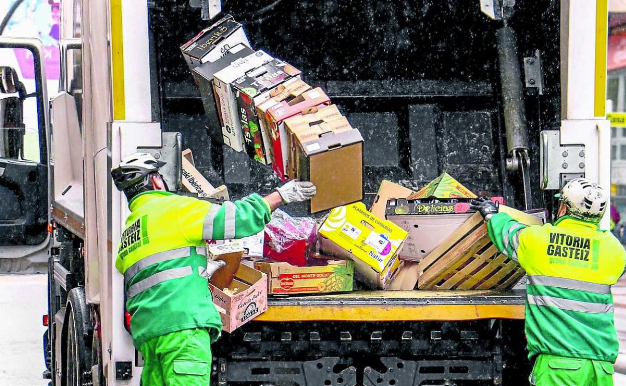 Dos operarios introducen basura en uno de los camiones de recogida.