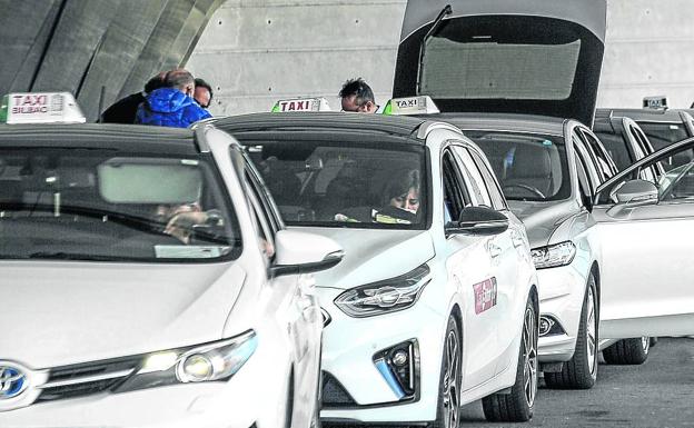 Imagen principal - Algunos de los 115 taxistas que trabajan en el aeropuerto aguardan la llegada de viajeros. Una pareja pide información a un ertzaina. La gran mayoría de las tiendas y bares del aeropuerto están cerrados.