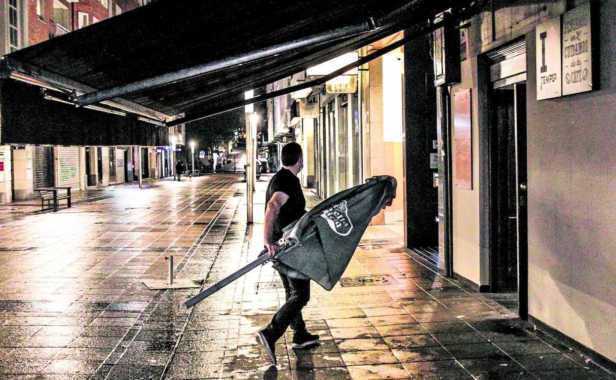 Un camarero, en la calle Fueros, recoge la terraza antes de cerrar el bar donde trabaja.