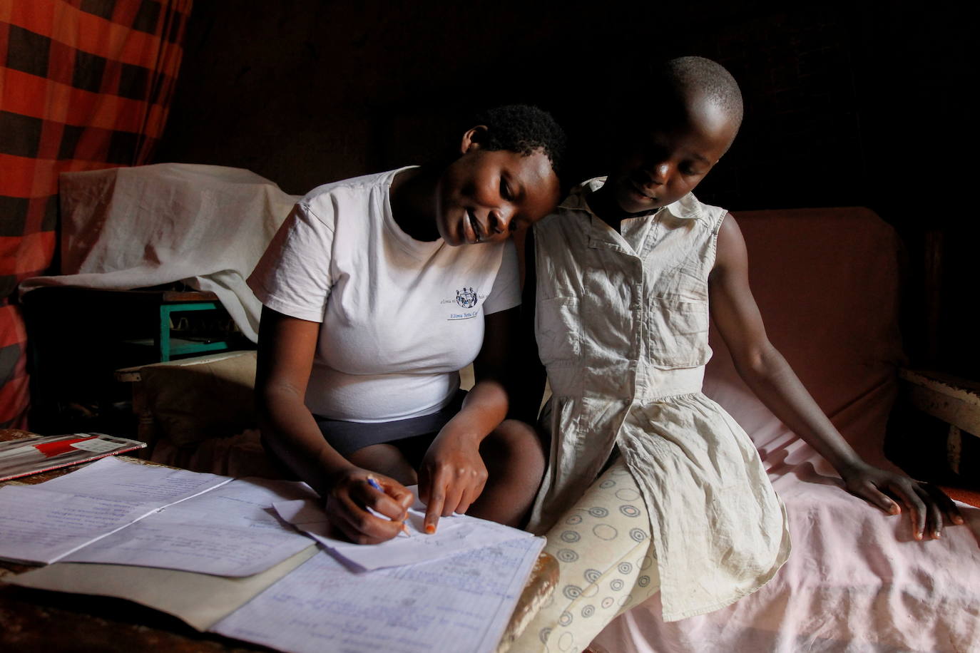 La estudiante de secundaria Jackline Bosibori, de 17 años, que tiene siete meses de embarazo, ayuda a su hermana menor Angela Moraa, de 12 años, con el trabajo escolar en su casa en la aldea de Lindi dentro de los barrios marginales de Kibera en Nairobi, Kenia.