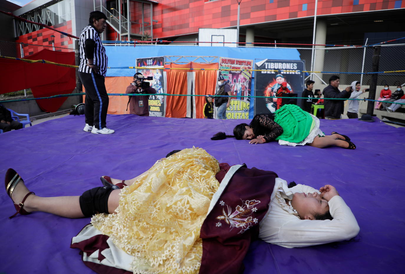 Luchadoras cholitas tras finalizar una pelea descansan en el suelo.