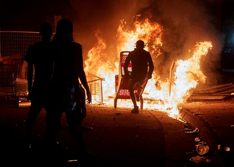 Los manifestantes se reúnen para ver los carros de la compra en llamas cerca del tercer recinto de la policía.